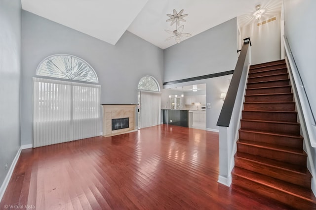 unfurnished living room featuring high vaulted ceiling, a fireplace, stairway, and wood finished floors