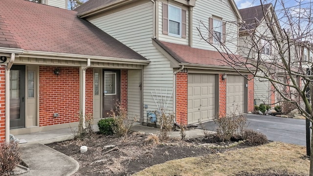 exterior space with a garage, roof with shingles, driveway, and brick siding