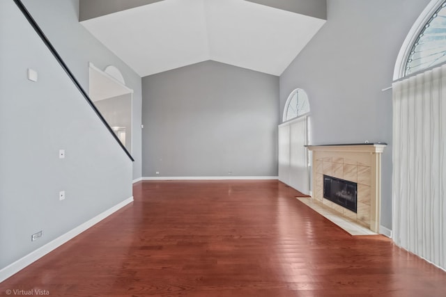 unfurnished living room with vaulted ceiling, a fireplace, baseboards, and wood finished floors