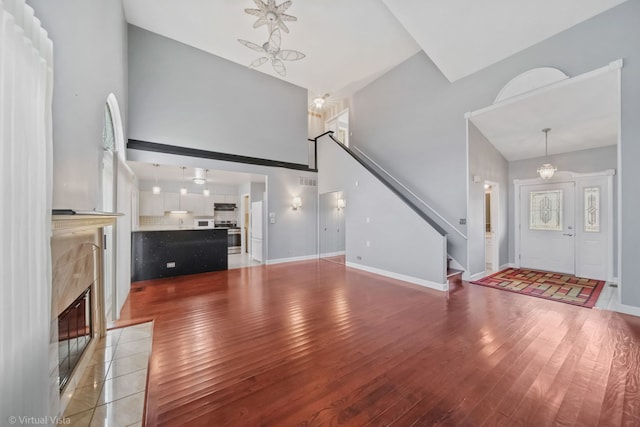 unfurnished living room with baseboards, stairway, light wood-style floors, a fireplace, and high vaulted ceiling