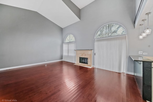 unfurnished living room featuring high vaulted ceiling, a tile fireplace, wood finished floors, and baseboards