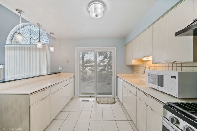 kitchen featuring light tile patterned floors, tasteful backsplash, light countertops, white microwave, and gas stove