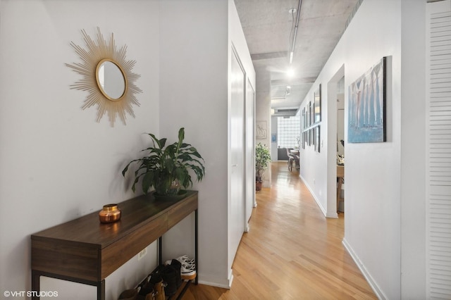 hall featuring rail lighting, baseboards, and light wood finished floors