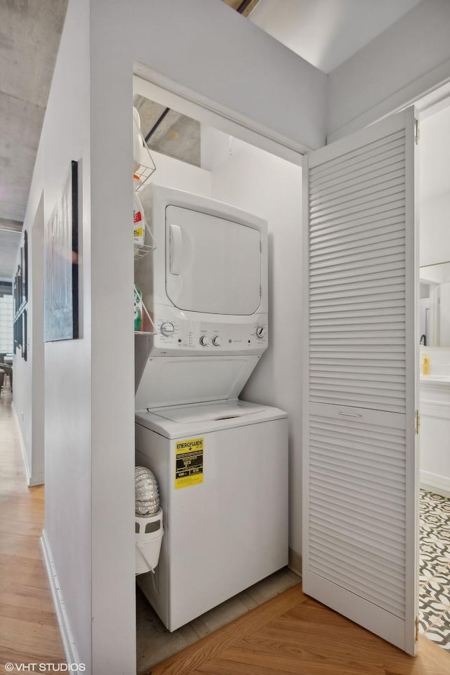 washroom featuring baseboards, light wood-style floors, laundry area, and stacked washing maching and dryer