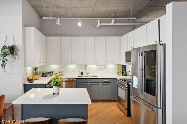 kitchen featuring light wood-type flooring, decorative backsplash, gray cabinets, stainless steel appliances, and a sink