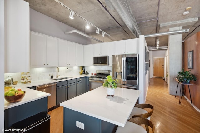 kitchen with light wood finished floors, a center island, a breakfast bar, appliances with stainless steel finishes, and a sink