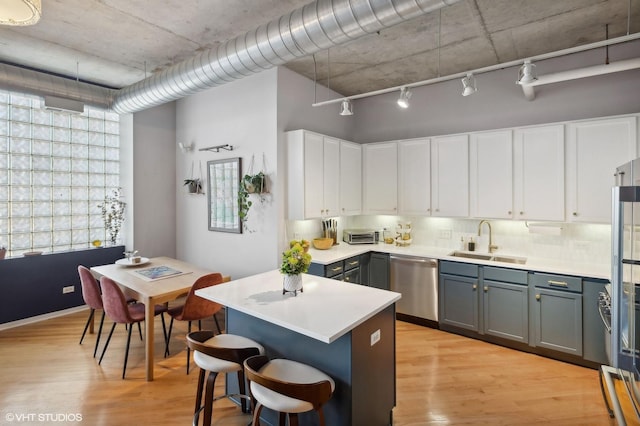 kitchen featuring a kitchen bar, light wood finished floors, a sink, light countertops, and dishwasher