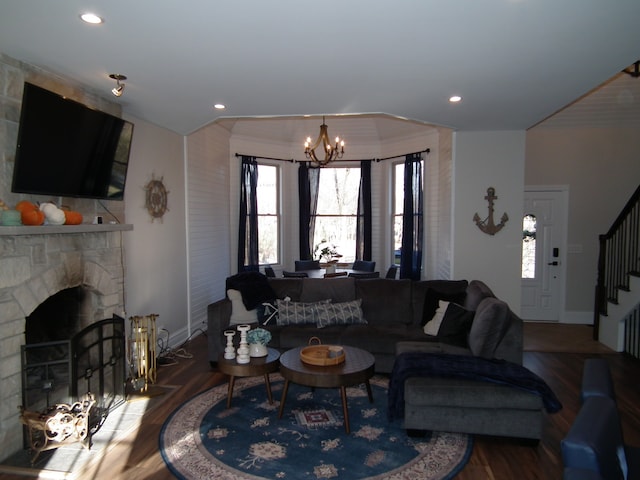 living room with a stone fireplace, wood-type flooring, ornamental molding, and an inviting chandelier