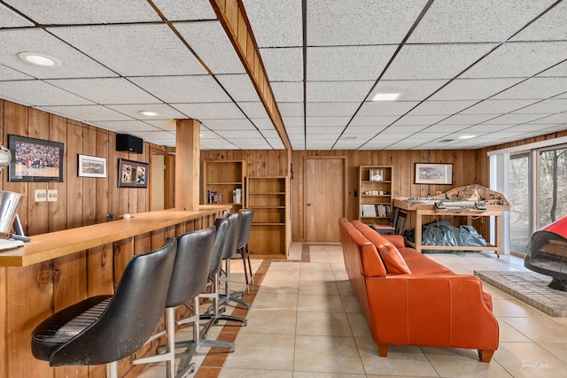 bar featuring wood walls, a drop ceiling, and light tile patterned floors