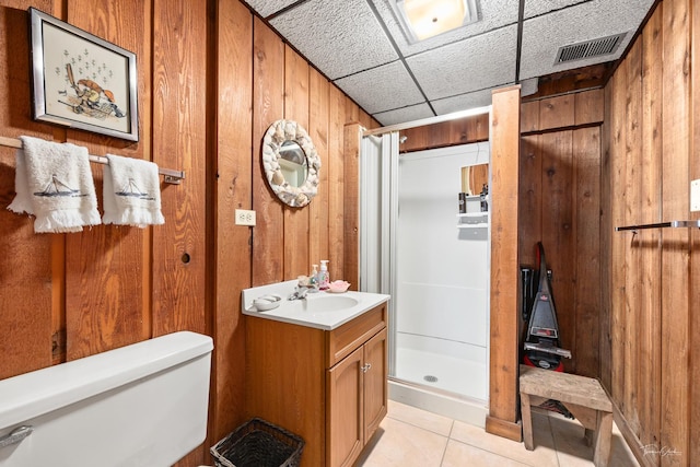 bathroom with a drop ceiling, walk in shower, tile patterned floors, wood walls, and vanity