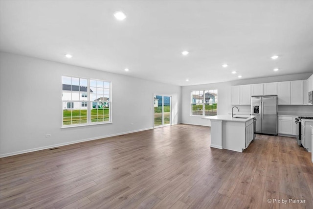 kitchen with a center island with sink, white cabinets, sink, light hardwood / wood-style flooring, and appliances with stainless steel finishes