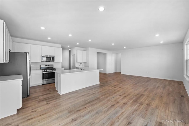 kitchen with a center island with sink, sink, light hardwood / wood-style flooring, appliances with stainless steel finishes, and white cabinetry