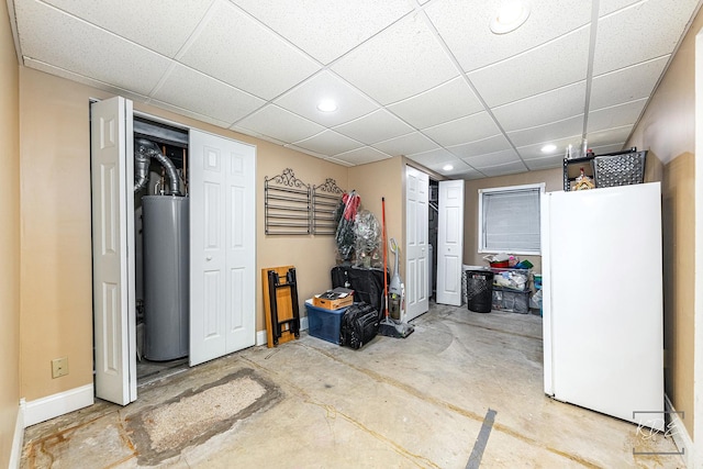 basement featuring white fridge, a drop ceiling, and water heater