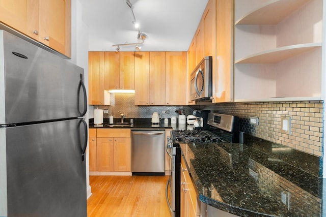 kitchen with sink, dark stone countertops, decorative backsplash, stainless steel appliances, and light wood-type flooring