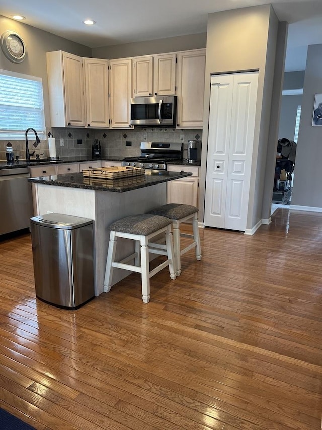 kitchen featuring dark wood-type flooring, appliances with stainless steel finishes, a center island, a kitchen bar, and decorative backsplash