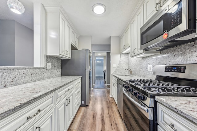 kitchen featuring white cabinets, light stone countertops, light wood-type flooring, a textured ceiling, and stainless steel appliances