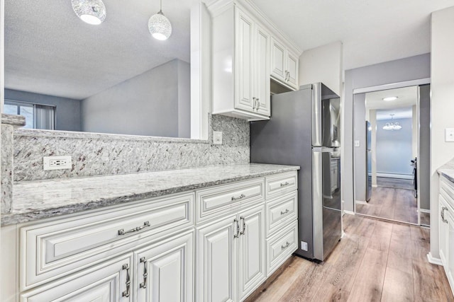 kitchen with stainless steel refrigerator with ice dispenser, decorative light fixtures, light wood-type flooring, white cabinets, and backsplash