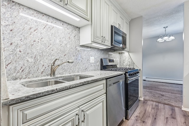 kitchen with sink, baseboard heating, a notable chandelier, appliances with stainless steel finishes, and light wood-type flooring