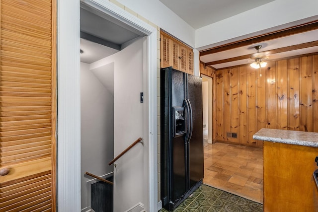 kitchen featuring black refrigerator with ice dispenser, wooden walls, dark parquet floors, ceiling fan, and beam ceiling