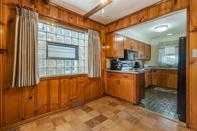 kitchen with wood walls, light stone countertops, sink, and black appliances