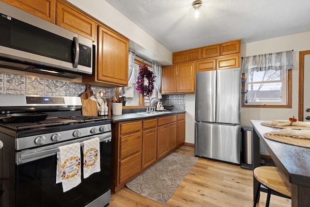 kitchen with sink, backsplash, light hardwood / wood-style floors, a textured ceiling, and appliances with stainless steel finishes