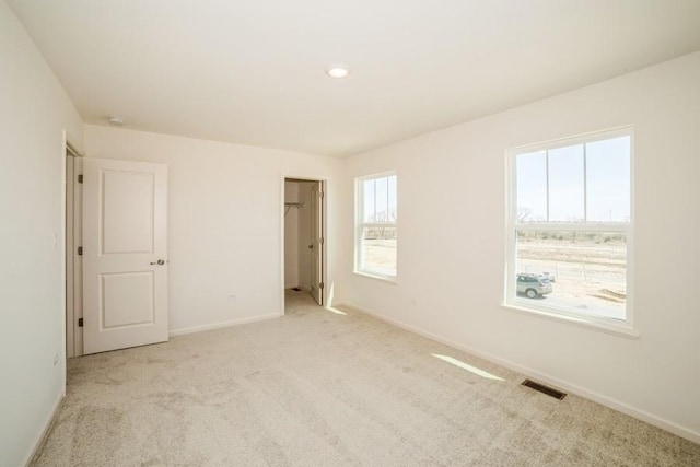 unfurnished bedroom featuring light colored carpet, a spacious closet, and multiple windows