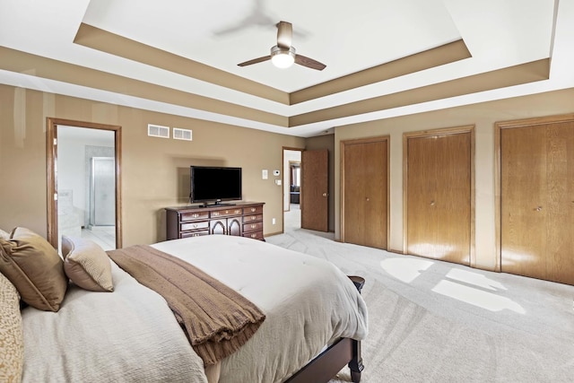 bedroom featuring multiple closets, connected bathroom, a tray ceiling, and light carpet