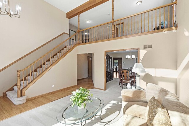 living room featuring an inviting chandelier, a towering ceiling, light hardwood / wood-style flooring, and beam ceiling