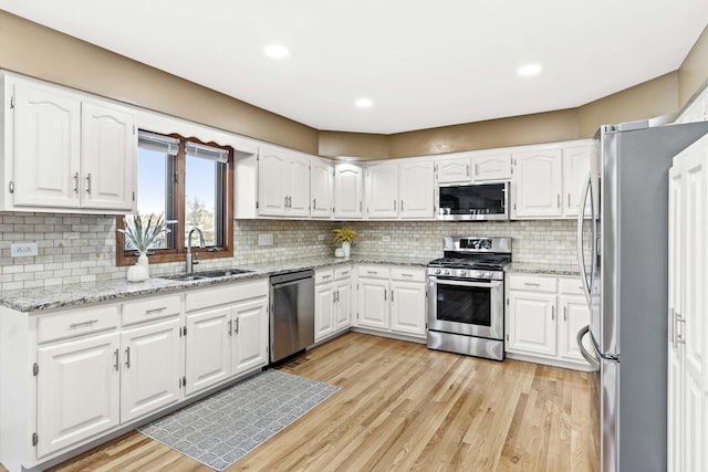 kitchen with sink, stainless steel appliances, white cabinets, and light stone countertops