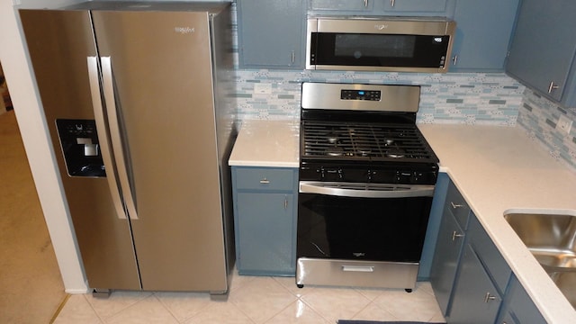 kitchen featuring tasteful backsplash, blue cabinetry, light tile patterned floors, and appliances with stainless steel finishes