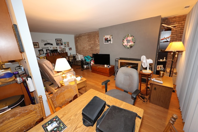 office area with light hardwood / wood-style flooring and brick wall