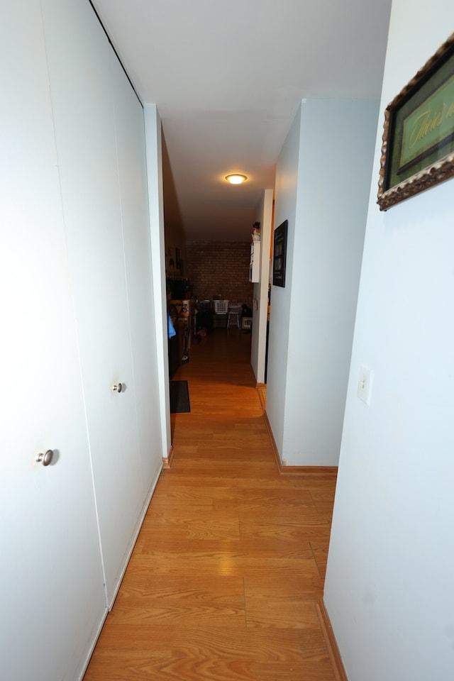 corridor featuring brick wall and light wood-type flooring