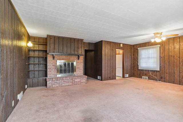 unfurnished living room with a brick fireplace, wooden walls, ceiling fan, and carpet