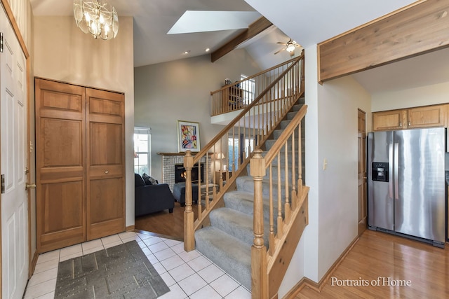 entryway with high vaulted ceiling, a brick fireplace, light hardwood / wood-style flooring, beam ceiling, and ceiling fan with notable chandelier