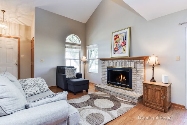 living room featuring a brick fireplace, a chandelier, hardwood / wood-style floors, and high vaulted ceiling