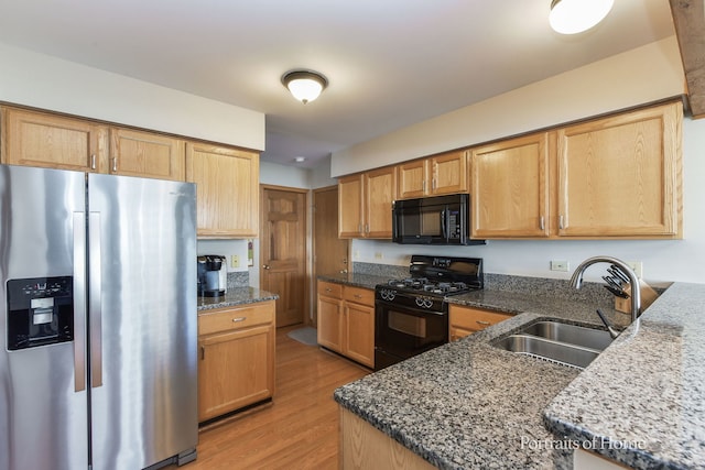 kitchen with sink, dark stone counters, light wood-type flooring, and black appliances