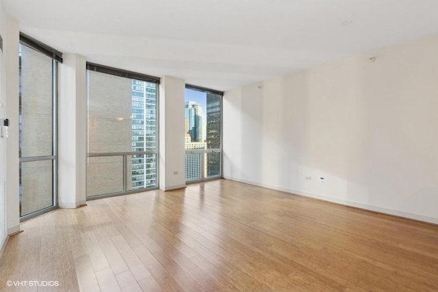 unfurnished room with a city view, light wood finished floors, a wall of windows, and baseboards