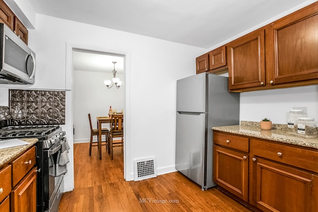 kitchen featuring light stone countertops, stainless steel appliances, decorative light fixtures, an inviting chandelier, and light hardwood / wood-style floors