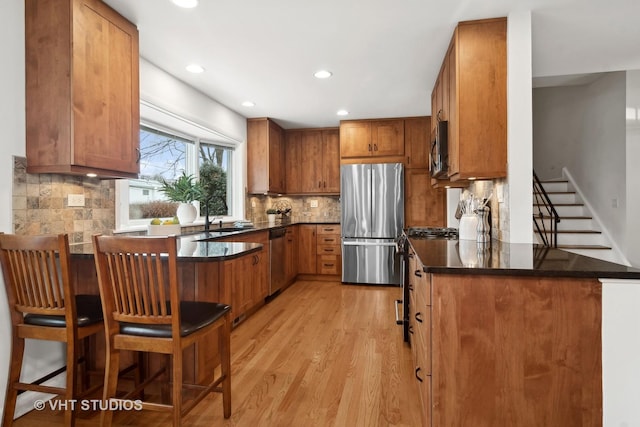 kitchen featuring kitchen peninsula, stainless steel appliances, light hardwood / wood-style flooring, and tasteful backsplash