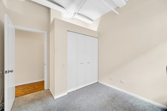 unfurnished bedroom featuring beam ceiling, carpet floors, and a closet