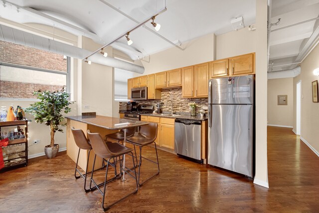 kitchen featuring a kitchen breakfast bar, backsplash, stainless steel appliances, dark wood-type flooring, and sink