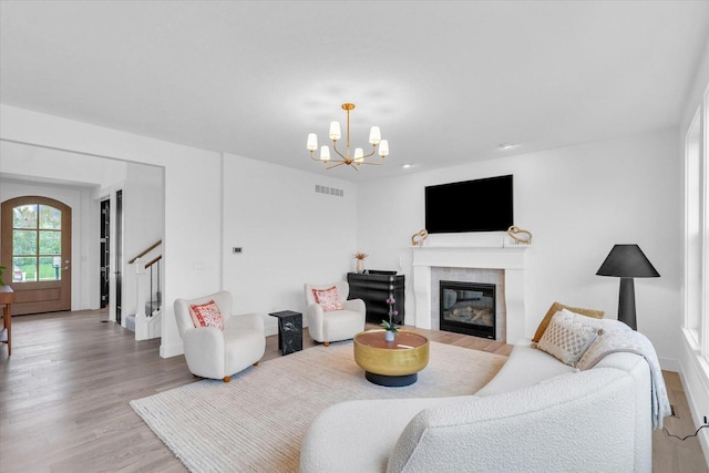 living room with a notable chandelier, visible vents, light wood-style flooring, a glass covered fireplace, and stairs