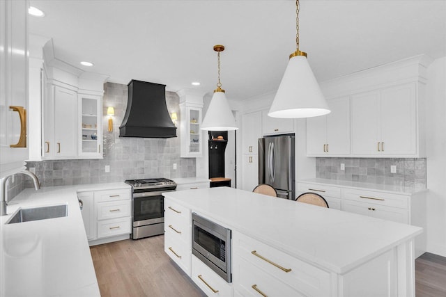 kitchen featuring stainless steel appliances, a sink, a center island, glass insert cabinets, and custom range hood