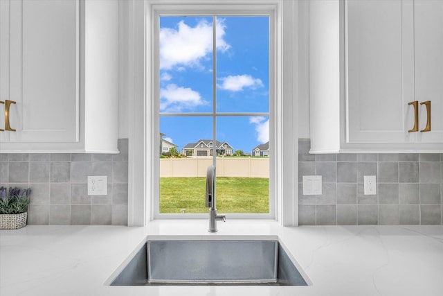 interior details with white cabinetry, a sink, decorative backsplash, and light stone countertops