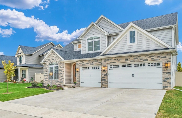 craftsman inspired home featuring a garage, a shingled roof, concrete driveway, stone siding, and a front yard