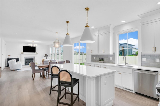 kitchen featuring a center island, decorative light fixtures, light countertops, stainless steel dishwasher, and white cabinetry