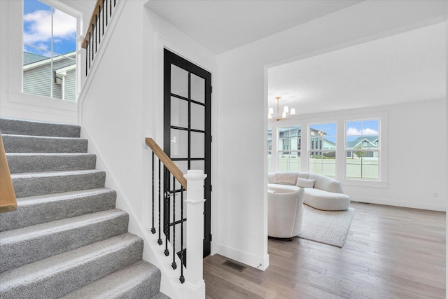 stairs featuring baseboards, wood finished floors, visible vents, and a notable chandelier