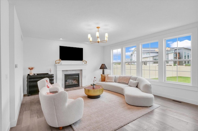 living area with a chandelier, a glass covered fireplace, a healthy amount of sunlight, and light wood-style flooring