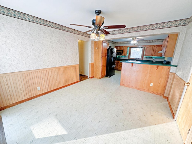 kitchen featuring kitchen peninsula, a kitchen breakfast bar, black refrigerator, ceiling fan, and wood walls