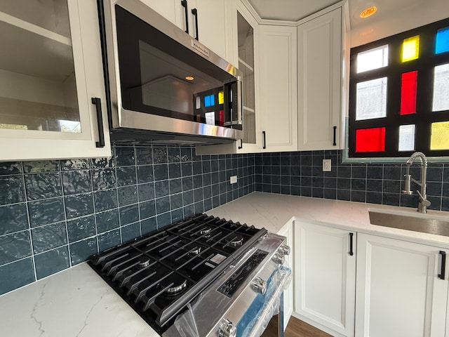 kitchen featuring appliances with stainless steel finishes, backsplash, light stone counters, sink, and white cabinets